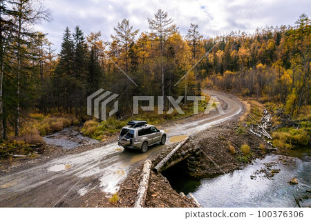SUV on wooden bridge over small mountain river. Autumn forest. 100376306