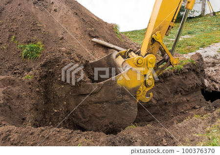 A bucket of excavator or bulldozer with a pile of earth digs a hole on the construction site close up A bucket of excavator or bulldozer with a pile of earth digs a hole on the construction site close up 100376370