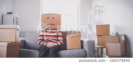 Tired sad woman with cardboard box on her head sitting on the sofa in her new house. Tired sad woman with cardboard box on her head sitting on the sofa in her new house. 100379840