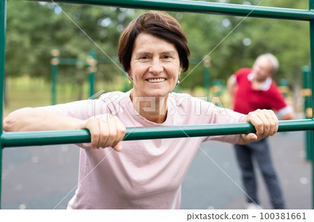 Aged woman doing exercises on sports bars in open-air sports area Aged woman doing exercises on sports bars in open-air sports area 100381661