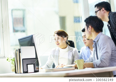 four young asian businesspeople meeting in office discussing business plan using desktop PC 100382149