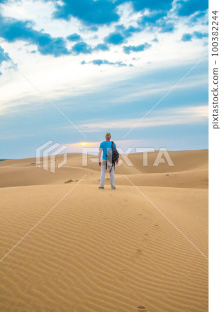 One man stands on a sand dune in the Kyzylkum desert at sunrise 100382244
