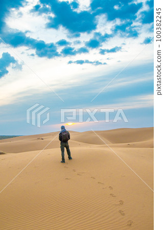 One man stands on a sand dune in the Kyzylkum desert at sunrise 100382245