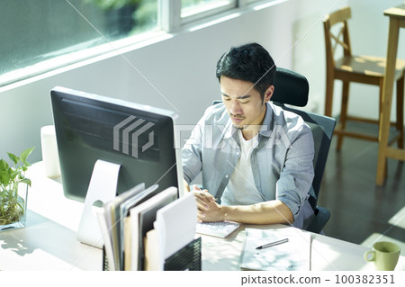young asian business man entrepreneur sitting at desk in office contemplating young asian business man entrepreneur sitting at desk in office contemplating 100382351