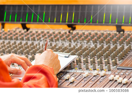 male songwriter hand writing a song on audio mixing console in recording studio. songwriting concept male songwriter hand writing a song on audio mixing console in recording studio. songwriting concept 100383086