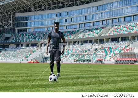 African American man playing football on the stadium field. A man runs with a soccer ball across the field. 100385432
