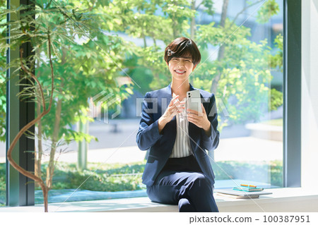 A middle-aged business woman in a suit operating a smartphone in the office Photography cooperation: LINK FOREST 100387951
