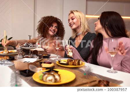 Three young cheerful intercultural women with alcoholic drinks standing in front of camera while enjoying home party in living room Three young cheerful intercultural women with alcoholic drinks standing in front of camera while enjoying home party in living room 100387957