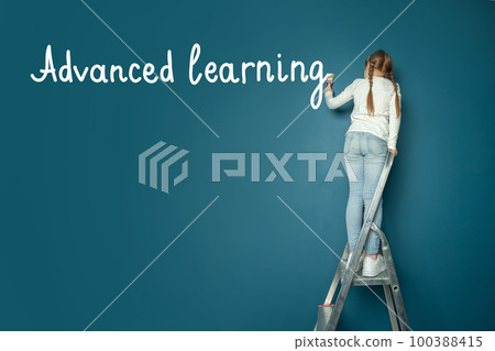 Girl painting blue wall with brush writing Advanced learning. School, education, learning concept Girl painting blue wall with brush writing Advanced learning. School, education, learning concept 100388415