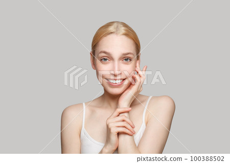Glamorous happy blonde woman touching her face isolated on grey background.  100388502