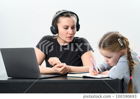 a young woman in headphones works on a laptop and exercises with her daughter at the same time. 100390693