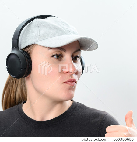 Portrait of a girl on a white background with wireless headphones and a cap on her head, copy space with emotional photo of a girl with headphones. 100390696
