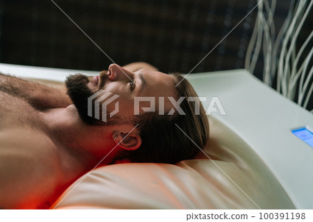 Closeup face of handsome young man lying relaxing on electric massage bed and enjoying spa treatment at luxury spa salon. Muscular male having rest enjoying wellness weekend, thinking looking up. Closeup face of handsome young man lying relaxing on electric massage bed and enjoying spa treatment at luxury spa salon. Muscular male having rest enjoying wellness weekend, thinking looking up. 100391198