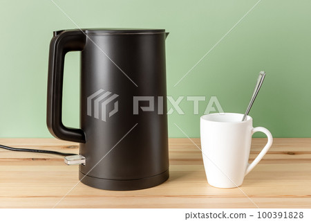 Matte black kettle and white mug on a wooden countertop. Matte black kettle and white mug on a wooden countertop. 100391828