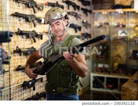 Man choosing rifle in airsoft shop 100392118