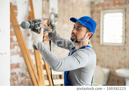 Builder in blue overalls working with pneumatic chisel hammer Builder in blue overalls working with pneumatic chisel hammer 100392223