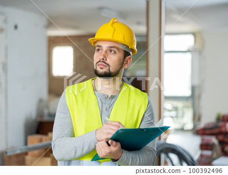 Builder making notes on indoor construction site 100392496