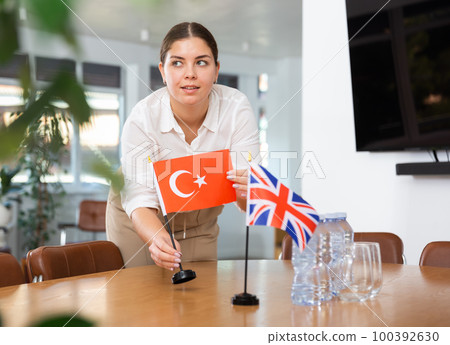 Young woman puts Turkish and UK flags on table 100392630
