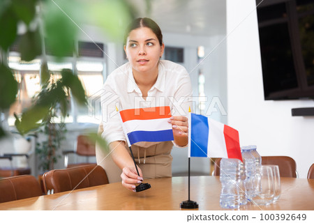 Young woman puts flags of Netherlands and France on table 100392649