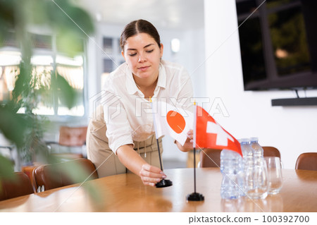 Positive young woman putting flag of Japan on the table with flag of Switzerland in conference room 100392700