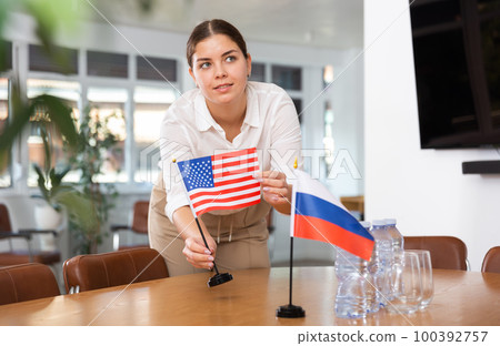 Preparing for business presentation - secretary places flags of Russia and USA on negotiating table 100392757