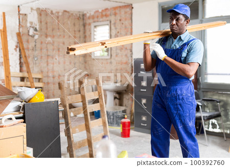 African american carpenter carrying wooden planks at construction site 100392760