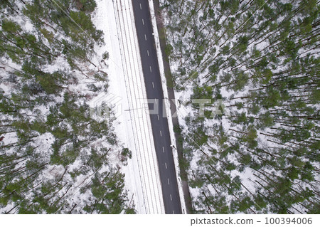 Aerial view on road in winter time, road surrounded with forest trees. Rural winter area. Top view landscape. shooting from drone. Snow covered road in winter forest Aerial view on road in winter time, road surrounded with forest trees. Rural winter area. Top view landscape. shooting from drone. Snow covered road in winter forest 100394006