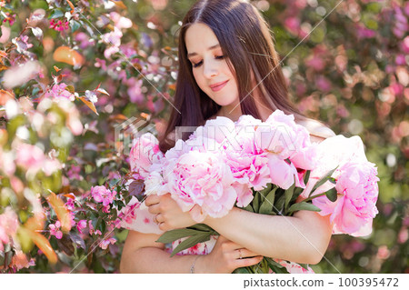 A happy beautiful girl holding a large bouquet of pink peonies 100395472