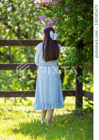rear view, girl in dress stands , with long hair, in the garden  100395473