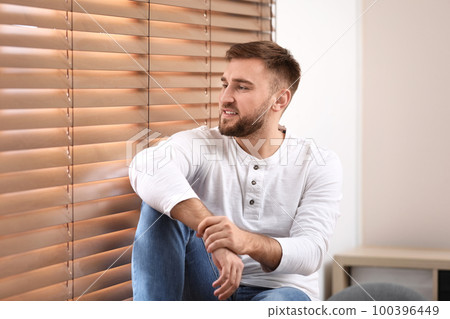 Handsome young man near window at home Handsome young man near window at home 100396449