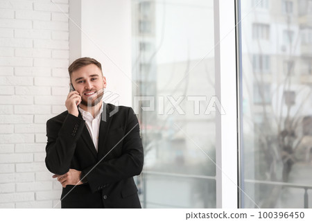 Young businessman talking on phone near window at home Young businessman talking on phone near window at home 100396450