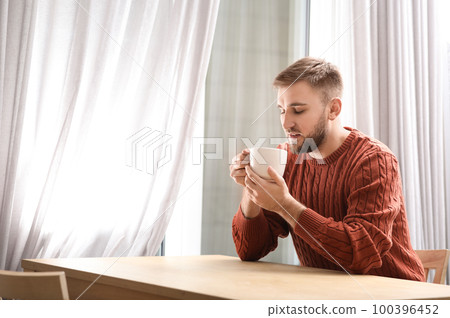 Young man with cup of hot drink near window at cafe 100396452