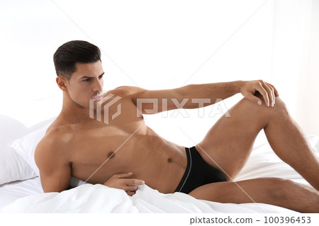 Handsome man in black underwear on bed indoors Handsome man in black underwear on bed indoors 100396453