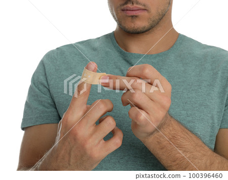 Man putting sticking plaster onto finger on white background, closeup Man putting sticking plaster onto finger on white background, closeup 100396460
