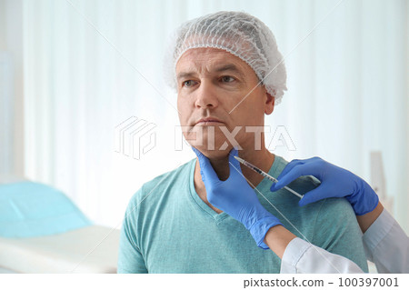 Mature man with double chin receiving injection in clinic 100397001