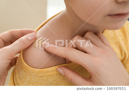 Mother putting sticking plaster onto son's shoulder indoors, closeup 100397051