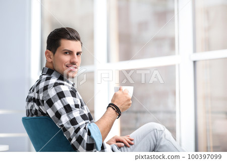 Man with cup of drink resting near window at home Man with cup of drink resting near window at home 100397099