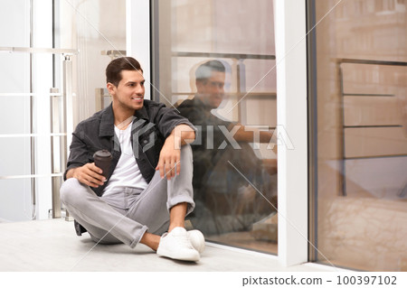 Handsome man with paper cup of coffee near window at home 100397102