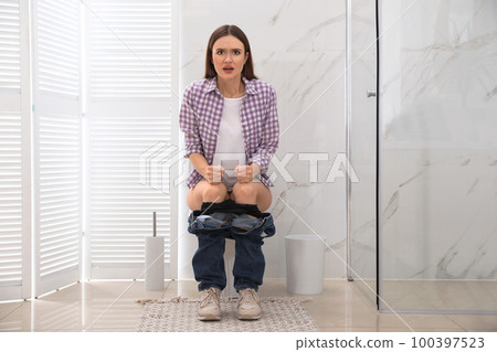 Woman suffering from hemorrhoid on toilet bowl in rest room 100397523