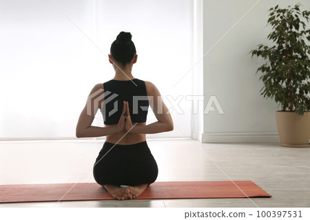 Woman practicing vajrasana with namaste behind back in yoga studio 100397531
