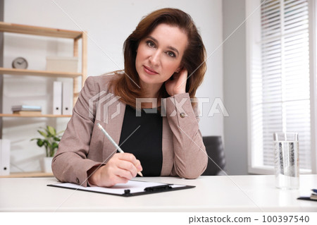 Portrait of psychotherapist with clipboard at table in office 100397540