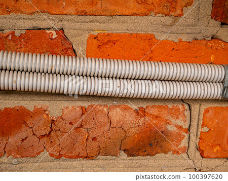 Electrical wiring in plastic corrugation on a brick wall. 100397620