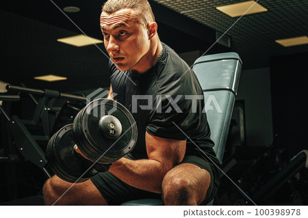 Muscular young man lifting weights in a dark gym 100398978