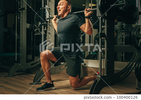 Fit man doing squats in a training machine 100400126