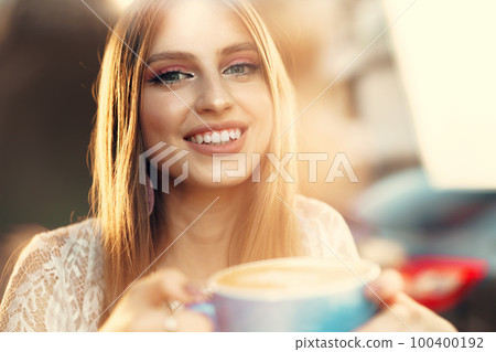 Portrait of a young woman having a cup of coffee and looking through the window 100400192
