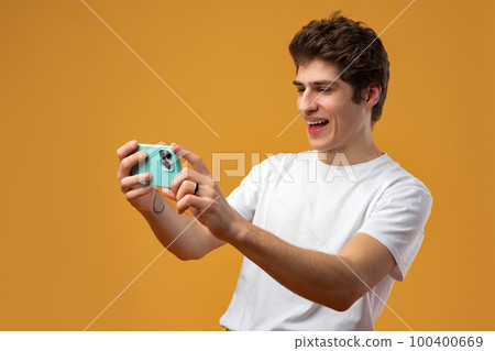 Young happy man looking at his phone against yellow background 100400669