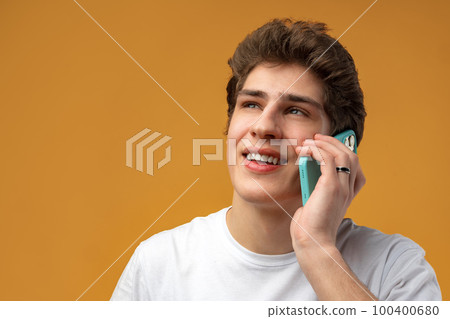 Portrait of young man talking on phone over yellow background Portrait of young man talking on phone over yellow background 100400680