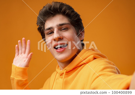 Young handsome man wearing casual hoodie waiving saying hello on yellow background Young handsome man wearing casual hoodie waiving saying hello on yellow background 100400899