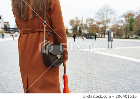 Woman wearing brown coat and stylish bag, posing back in the city Woman wearing brown coat and stylish bag, posing back in the city 100401536