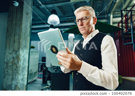 Handsome mature businessman using his digital tablet in the office Handsome mature businessman using his digital tablet in the office 100402076